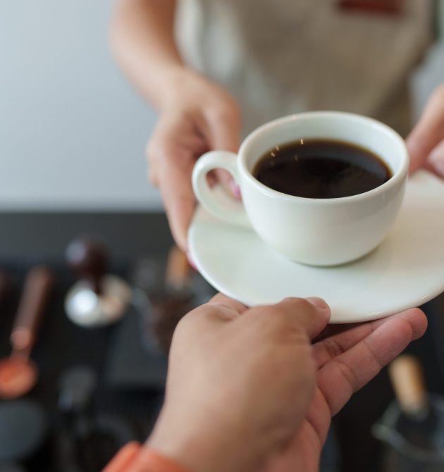 Barista handing a cup of black coffee to a customer in a coffee shop