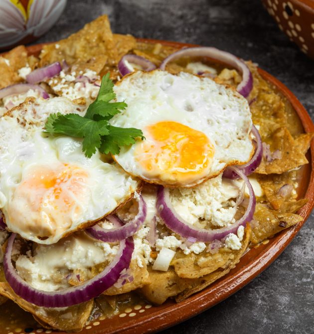 Chilaquiles, typical Mexican food, served in a clay dish with fried eggs and bread.