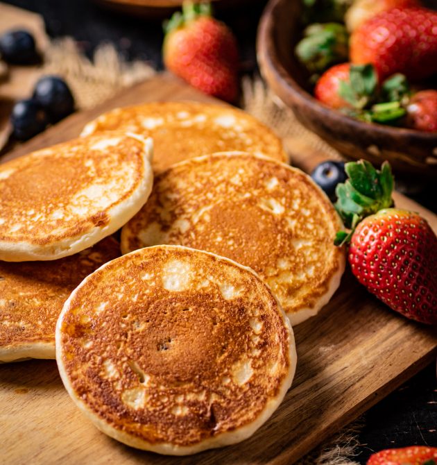 Pancakes on a wooden cutting board with honey and berries. Against a dark background. High quality photo