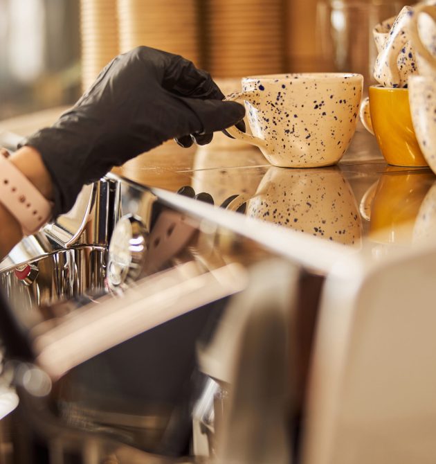 Close up of a hand in black rubber glove taking a cute cup from the warming rack of a coffee machine